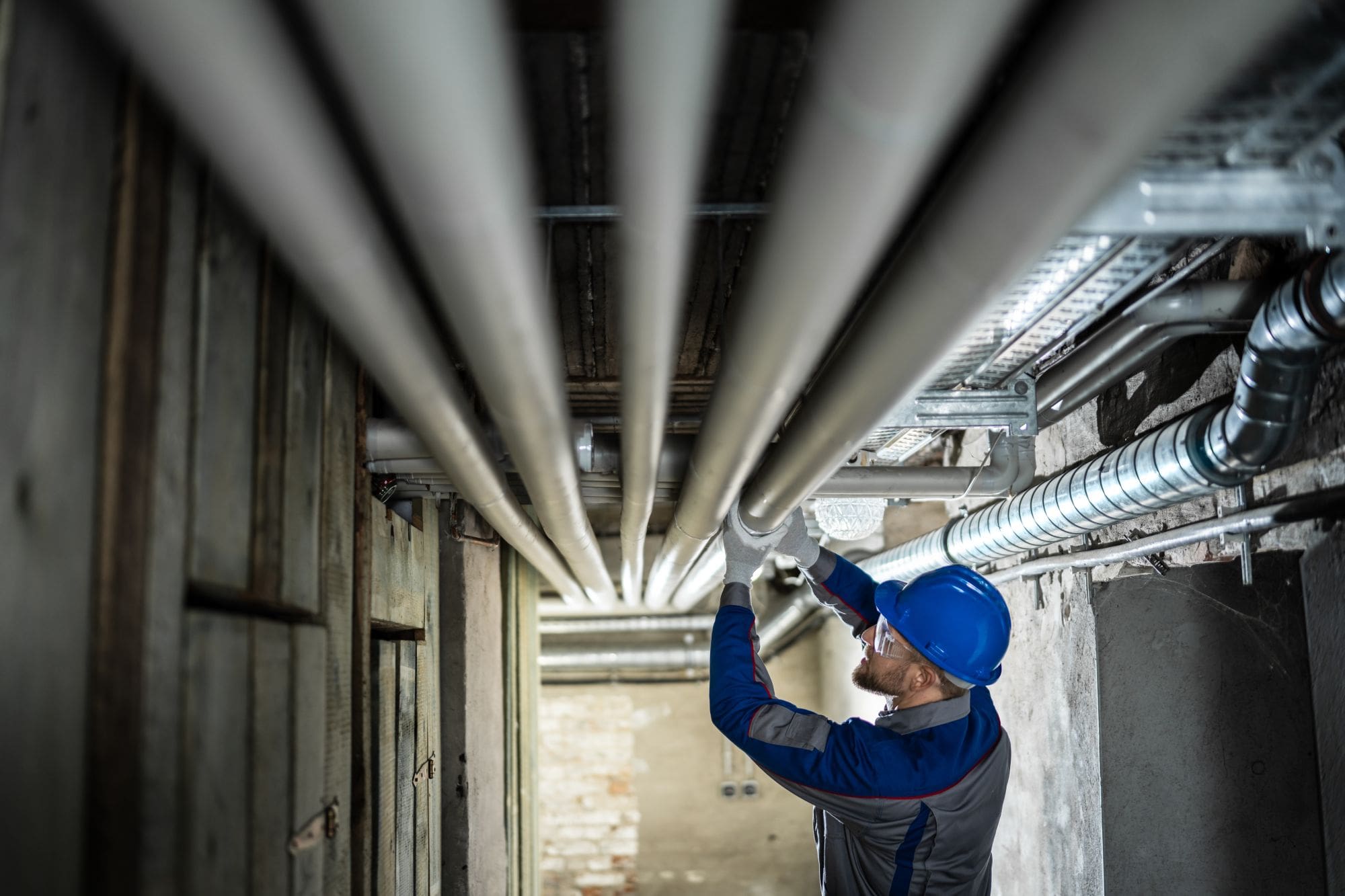 Worker inspecting plumbing pipes under a building